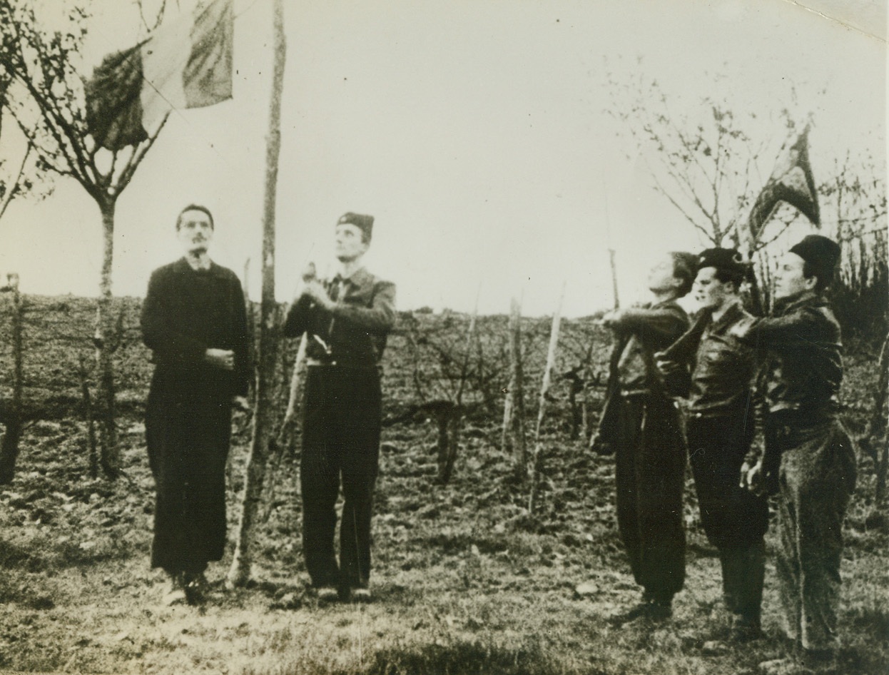 First Photos of French Underground, 3/13/1944. This photo, smuggled out of France and which just reached the U.S., is from a movie film made at one of the secret bases of the Maquis—French guerillas of the Underground who are fighting in the Savoy mountain regions. This is one of the first photos ever to reach the U.S. of the routine life of the guerillas before Darnand, the Himmler of France, launched his main attack on them early last February. These Maquis have forced the Germans to keep 6,000 troops in the Haute Savoie district, and are laying a solid foundation of offensive aid for the coming Allied invasion. Here, at a Maquis base, the day begins with the traditional French military ceremony of saluting the Tricoleur. Passed by censors. Credit: ACME;