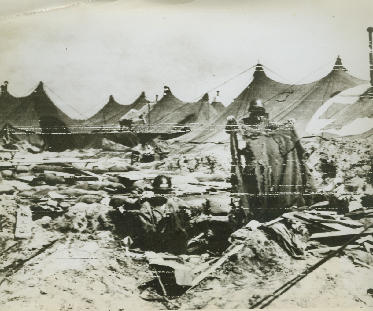 HOSPITAL [illegible], 4/8/1944. ANZIO, ITALY—Surveying the damage done to an American evacuation hospital at Anzio when German shells pounded the mercy encampment mercilessly, are: (left to right) Pvt Tom Botley and T/5 Jack Horn, both of Chicago, Ill. The latter holds a shrapnel-riddled hospital blanket.Credit: Signal Corps Radiotelephoto from Acme;