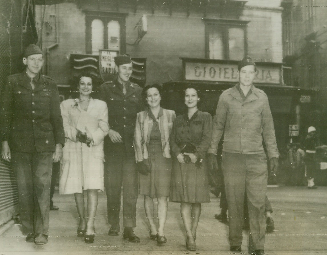 Time Out from War, 4/10/1944. NAPLES, ITALY – These U.S. soldiers take time out from the battle field to inject a little American tradition on to the streets of Naples, Italy. Walking along Via Roma with three local signorinas in typical Easter parade fashion are Pfc. Arnold Middendorf, Dubuque, Iowa, Pfc. Walter Sakala, Newark, N.J. and Pfc. Don Allen, Woonsocket, S.D. Credit Line (OWI Radio Photo from Acme);