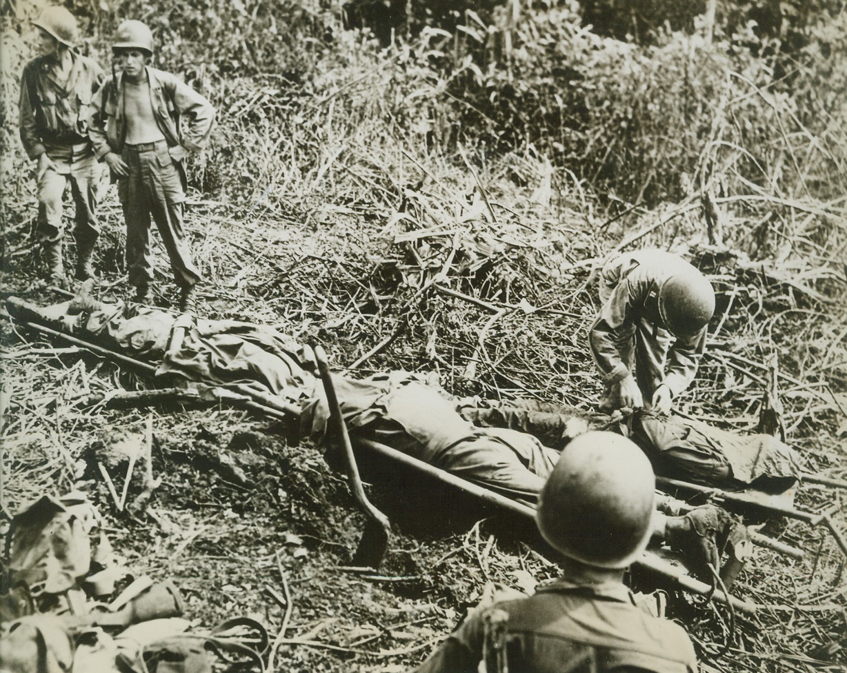 THEY DIED FOR VICTORY, 4/19/1944. ADMIRALTY ISLANDS—These three heroic Americans gave their lives so that the Japs might be driven from the Admiralty Island and a new step taken on the road to victory in the Pacific. They lie on litters at a first aid station in the Papitalia Area, where they died from battle wounds. Four of their buddies prepare them for removal to the rear. Credit: Signal Corps photo through OWI from Acme;