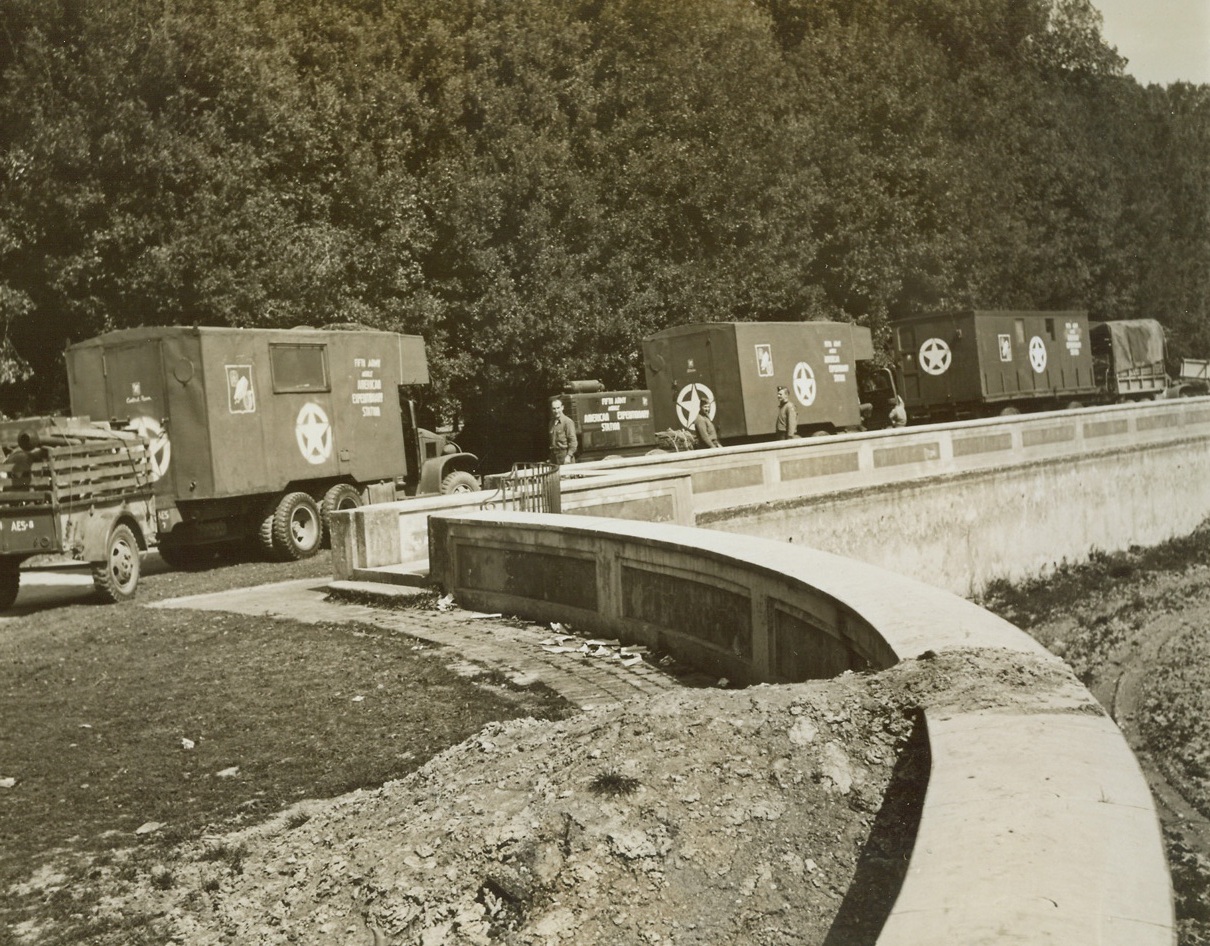 Mobile Radio Station “Gets Around”, 4/19/1944. Italy – War weary men and women of the Allied Fifth Army in Italy are mighty proud of their mobile radio station, officially known as the Fifth Army Mobile American Expeditionary Station, which gets its music and its “big time” programs to them wherever they are – the front lines, or in rest camps. The hard working crew that moves the station’s ten-unit “circus caravan” of jeeps and trailers, and 2 ½ ton trucks to various points in the combat area making sure that every group is reached at least once a day, have the moving operation down to a fine point. They can take the station down, move it 50 miles (which is the range of the transmitter), and set it up again, all within less than two hours. Here, the “Voice of the Fifth Army” is all packed up and ready to move. Salvaged enemy equipment and material played a big part of constructing the outfit. (Passed by Censors) Credit: ACME photo by Sherman Montrose for the War Picture Pool;