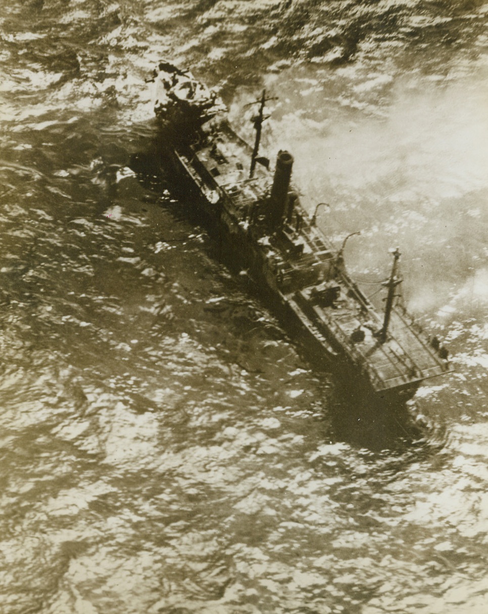 Downed Jap Cargo Ship, 4/8/1944. Eniwetok – Strafed, bombed and sent to the bottom by U.S. Navy raiders at Eniwetok Atoll, in the Marshall, in January 30th, this 2500-ton Jap cargo vessel smokes and tosses on the water during the attack.  The single gun that the ship carried for protection is located forward in a “tub” on the high prow.  Photo was made as a dive bomber swooped down to deliver the death blow. Credit line (Official U.S. Navy….);