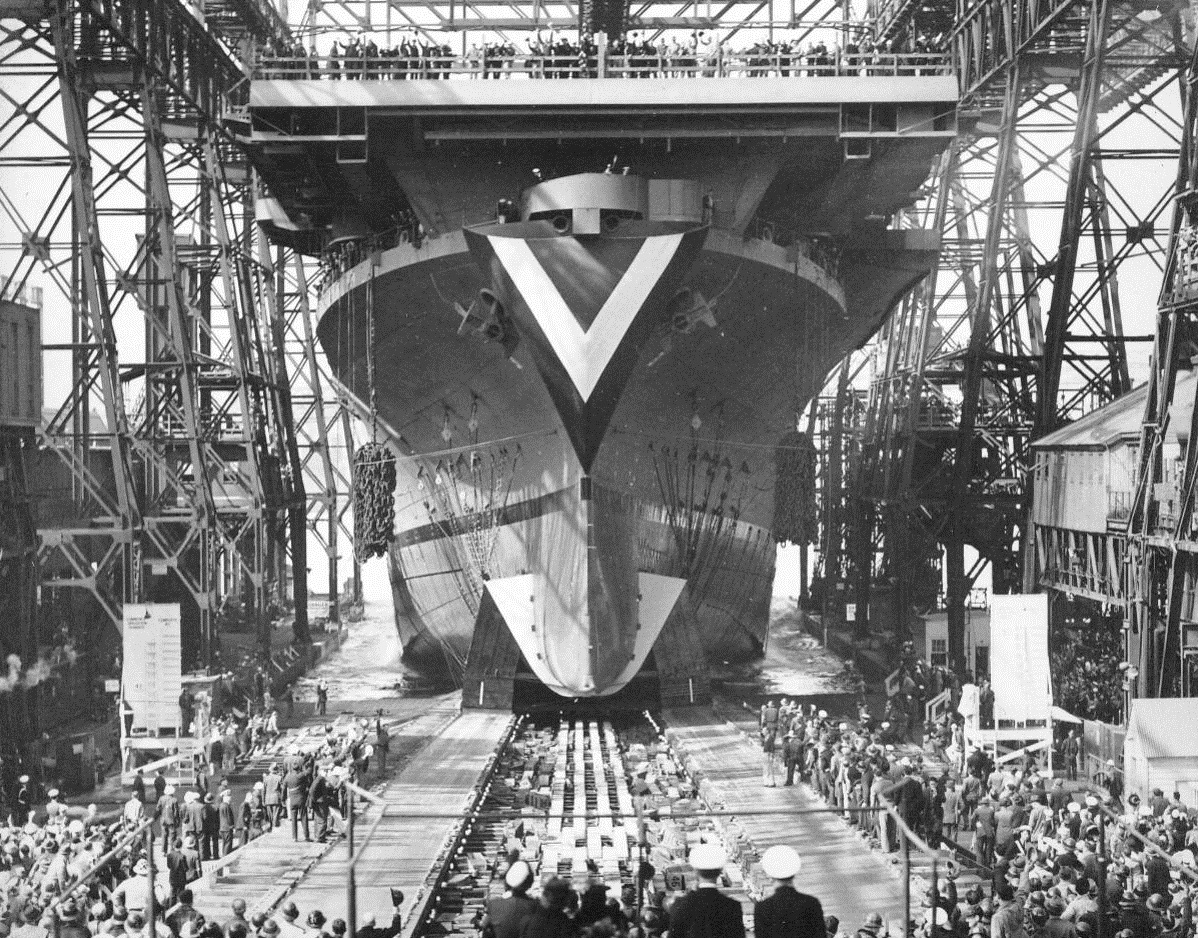 Open Aircraft Carrier Is Launched, 4/29/1944. New York City – Sliding down the ways under the impetus of 44,200 pounds of grease, the USS Don Homme Richard was launched at the Navy Yard this afternoon. The super aircraft carrier, which will house about 80 planes, including torpedo and scout bombers, is the thirteenth Essex class carrier to be launched since the U.S. entered the war. The ship, 850 feet long, is the namesake of John Paul Jones’ flagship, which had a keel length of 74 feet. Mrs. John S. McCain of Washington, wife of Admiral McCain, sponsored the carrier. Mrs. Frank Blasdel of Brooklyn and Mrs. Allen Raymond, of New York City, served as the matrons of honor.  4/29/44 (ACME);