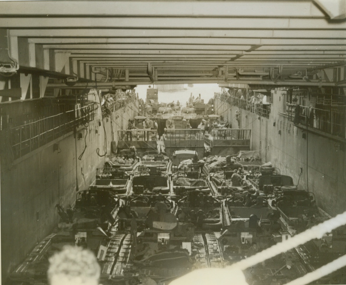 WELL LOADED, 5/8/1944. NEW GUINEA – The LSD (Landing Ship Dock) is shown somewhere in New Guinea, with its well deck loaded down with small craft. Included are LST (Landing Ship Tanks), Ducks, Buffaloes, and LSM (Landing Ship Mechanized). The smaller craft leave the mother vessel, water borne. In the recent invasion of Hollandia, Dutch New Guinea, there were Jap airplane engines, heavy guns, trucks, tractors, and other supplies, but few Japs. Our forces encountered minor opposition and are now at work wiping out the 60,000 Jap troops cut off from reinforcement and supply somewhere between Aitape and Hollandia. Credit: ACME photo by Tom Shafer, War Pool Correspondent;