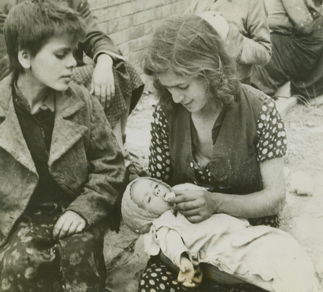 SUGAR BABY—A REFUGEE, 5/31/1944. ITALY—An Italian mother feeds her child a piece [illegible] on returning to Minturno after the [illegible] occupation of the town. Officials of the [illegible] Military Government are taking care of [illegible] Italian civilian refugees. Credit: Acme;