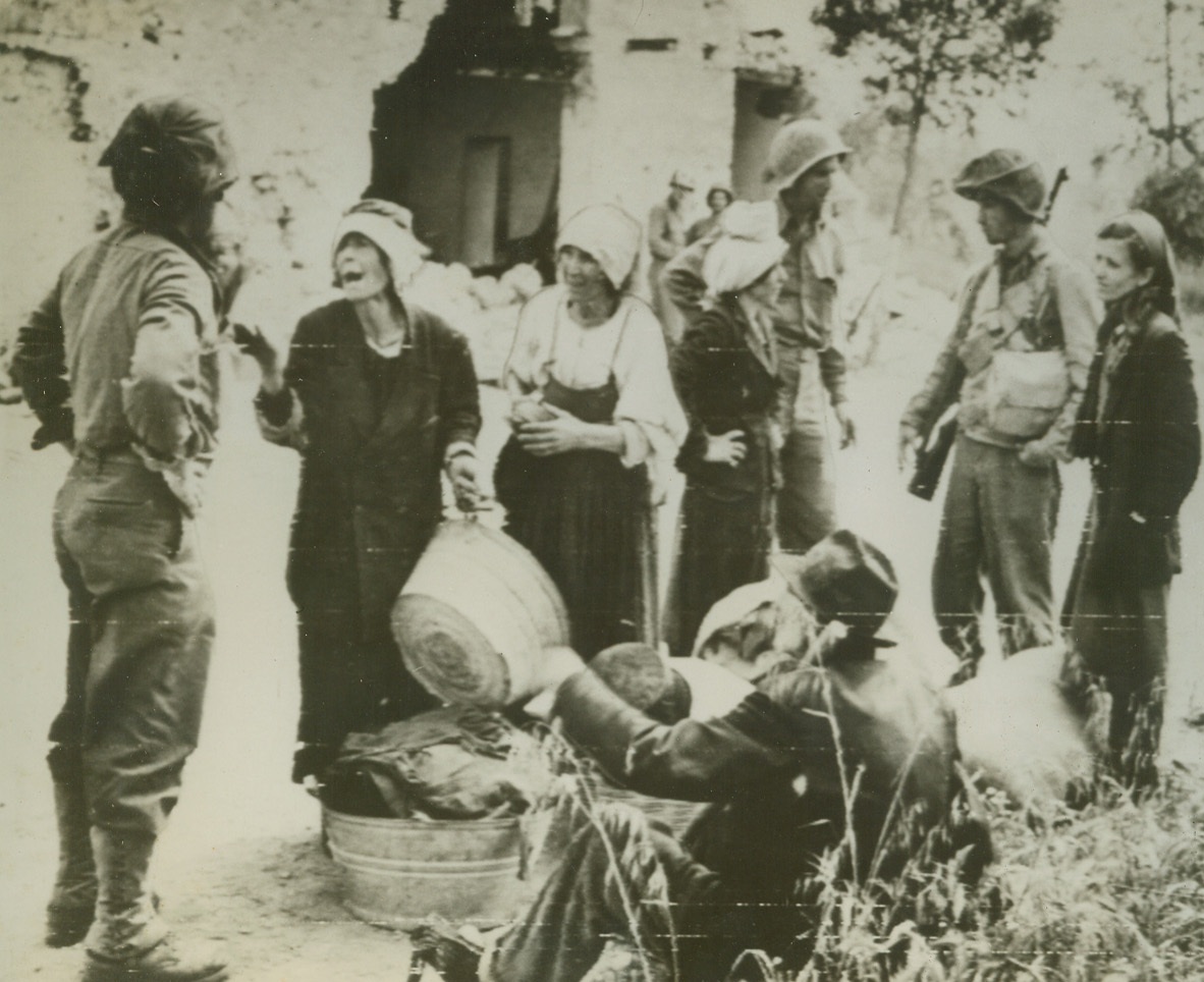 TRIBULATIONS OF AN AMERICAN INFANTRYMAN, 5/26/1944. ITALY—American infantrymen are stopped on the Appian Way and bombarded with questions by confused Italian refugees from nearby Formia. Note the woman on the left gesturing wildly. She wears a man’s double-breasted jacket. Credit: Acme photo by Charles Seawood, War Pool Correspondent via Army Radiotelephoto;