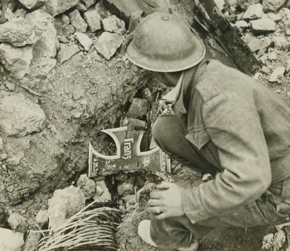 GRAVE IN RUINS OF MONASTERY, 5/25/1944. CASSINO, ITALY—an Allied soldier stoops to examine the grave of a Nazi warrior whose body lies beneath a pile of broken glass and rubble amid the ruins of the famous Benedictine monastery. Used as a fortress by the Germans, the ancient house of worship was the target for long and intense Allied aerial and long range artillery bombardment. Credit Line—WP—(ACME);