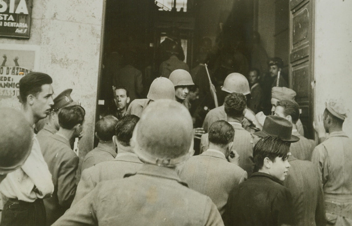 Lone Fascist Wages Own War, 6/24/1944. ROME, ITALY—When the American forces entered Rome, they were greeted by an unseen enemy. One lone fascist sniper opened fire on the soldiers from the window of an apartment house, but he was quickly nabbed by the Yanks. Here American soldiers force their way through a crowd of curious civilians into the lobby of the apartment house from which the sniper fired on the soldiers from an upper window. Credit:  Canadian Official Photo from ACME.;