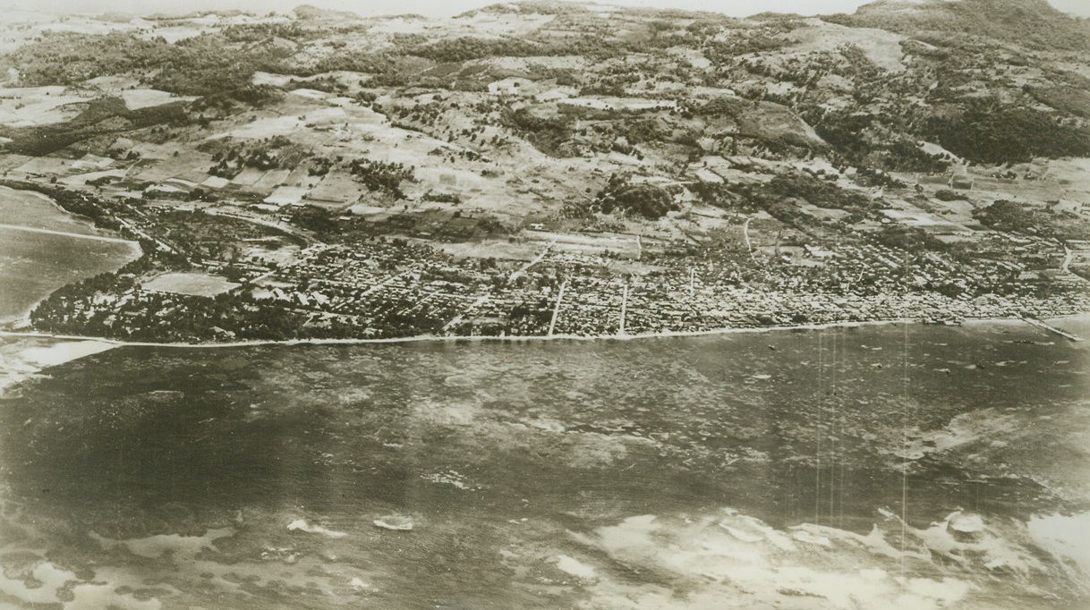 Yanks Reach Saipan Capital, 6/23/1944. Saipan, Marianas – This is an airview of Garapan, capital city of Saipan Island whose entire southern section is now in the hands of the Americans. Yank troops are now on the outskirts of the capitol and largest city, whose industries include a chemical plant and cannery. The large building to the left of Government Pier (right) is Japanese Administration Building. Enemy counter attack to the right of this area was repulsed by out forces. Credit: US Navy photo from ACME;