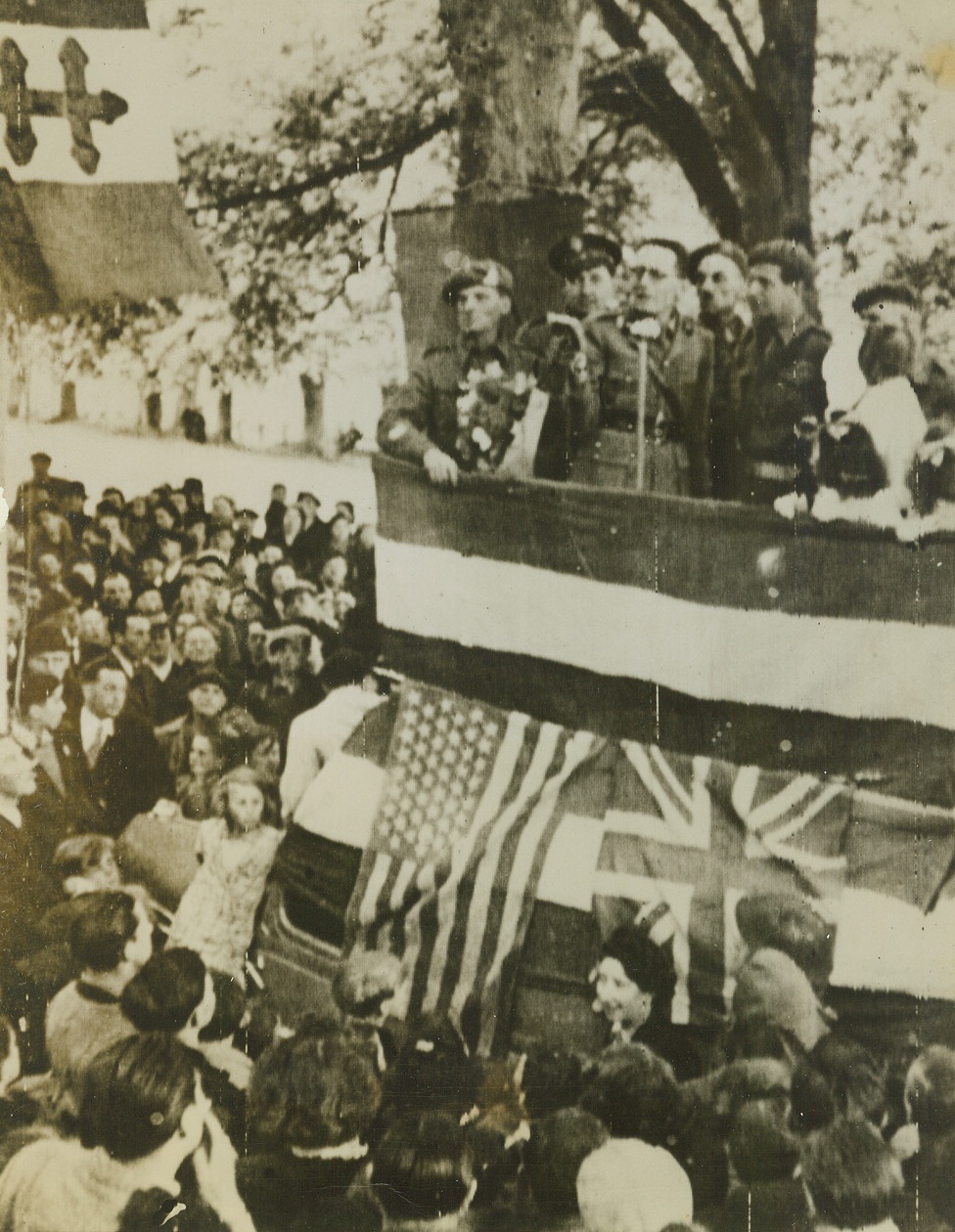 CELEBRATING FREEDOM, 6/12/1944. FRANCE—Allied officers and French war correspondents address the liberated civilians of Bayeux, the first town captured in the invasion of France. British and American flags decorate the speakers’ platform. The Allies have moved up the Normandy Peninsula to capture and threaten Cherbourg.  Credit (Signal Corps Radiotelephoto from ACME);