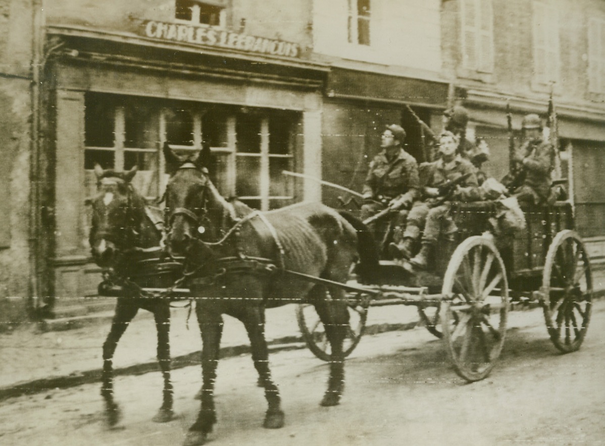 BACK TO “HORSE AND BUGGY” DAYS, 6/12/1944. ST. MERE EGLISE, FRANCE—Although they arrived in France by way of the most speedy, modern means of transportation, these paratroopers of the Allied invasion force revert to the “good ole days” as they jog along behind a horse and wagon. The field wagon was used by the Nazis when they ran short of vehicles. Credit (ACME Photo via Signal Corps Radiotelephoto);