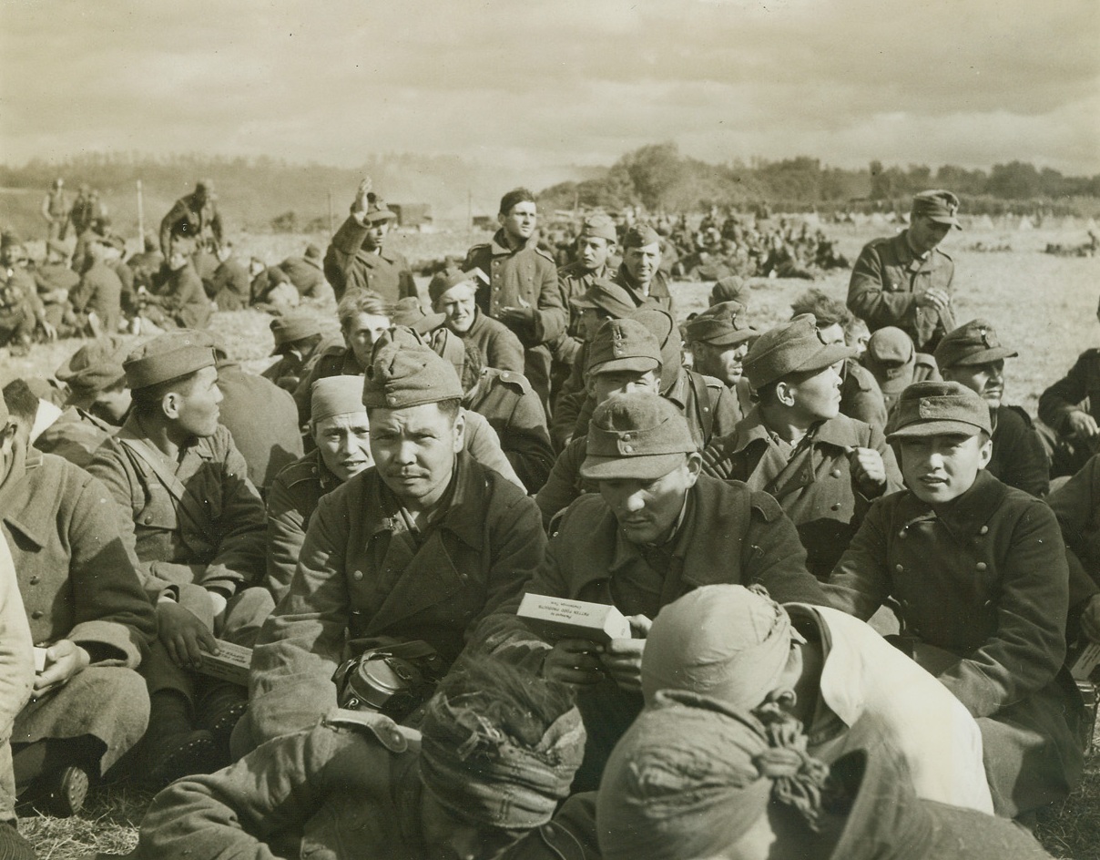 Captured with Nazis, 6/15/1944. France – Visible among the faces of these men, captured by the Allied liberation forces in Normandy, are Chinese and Mongolian types. Reports from Allied Headquarters indicate that Japanese also were among those fighting for the Nazis. At least, these men, (above), seem happy that they no longer have to fight for the German “Super Race.” Passed by censors. Credit: Acme photo by Bert Brandt for War Picture Pool;