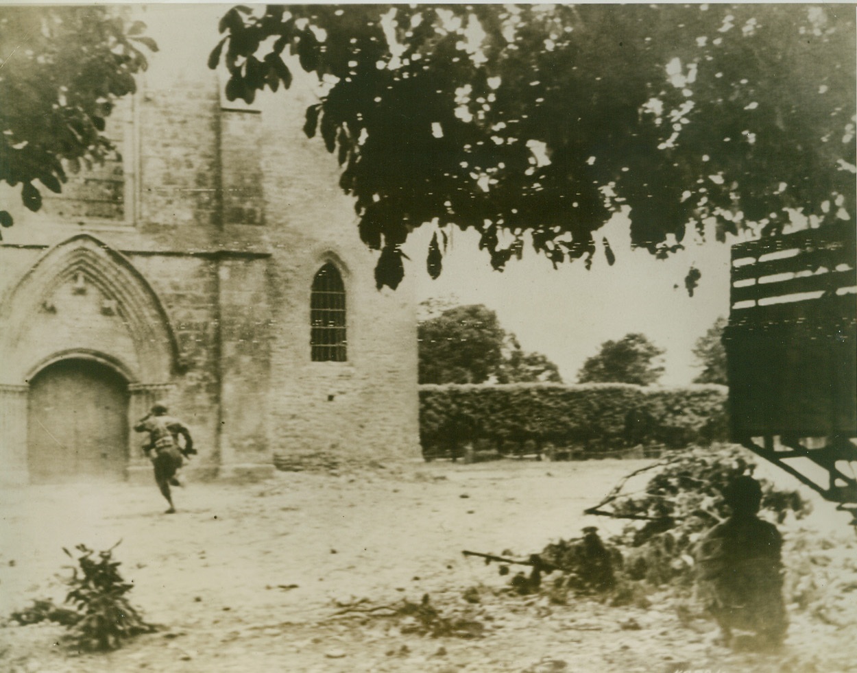 Routing Nazi Sniper, 6/12/1944. France—This dramatic picture tells the story of the courage of the Allied fighters in France and their determination to wipe out Nazi troops where ever they may find a hole occupied by an enemy rat. Here, in a desperate attempt to get a German sniper hidden in a church in the center of St. Mere Eglise, an infantryman dashes towards the sniper’s next while another Allied fighter, right, covers him. Credit: Army radiotelephoto from ACME;