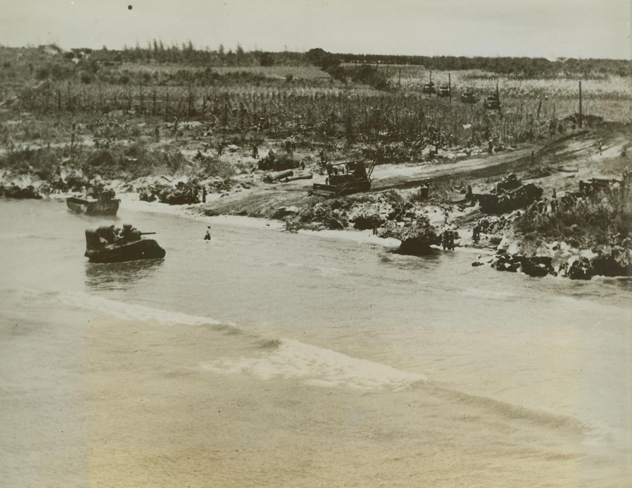 Marines Push Forward on Tinian, 7/28/1944. , Marianas Is. – With monotonous regularity – for the Japanese on the Marianas Islands – the Marines land again.  This time it is Tinian, less than three miles from Saipan, and the third in the group to be invaded in less than six weeks.  Tanks roar ashore from landing craft, drive up beach road gouged out by a bulldozer toward island’s vital airfields.Credit line Marine Corps Photo from ACME;