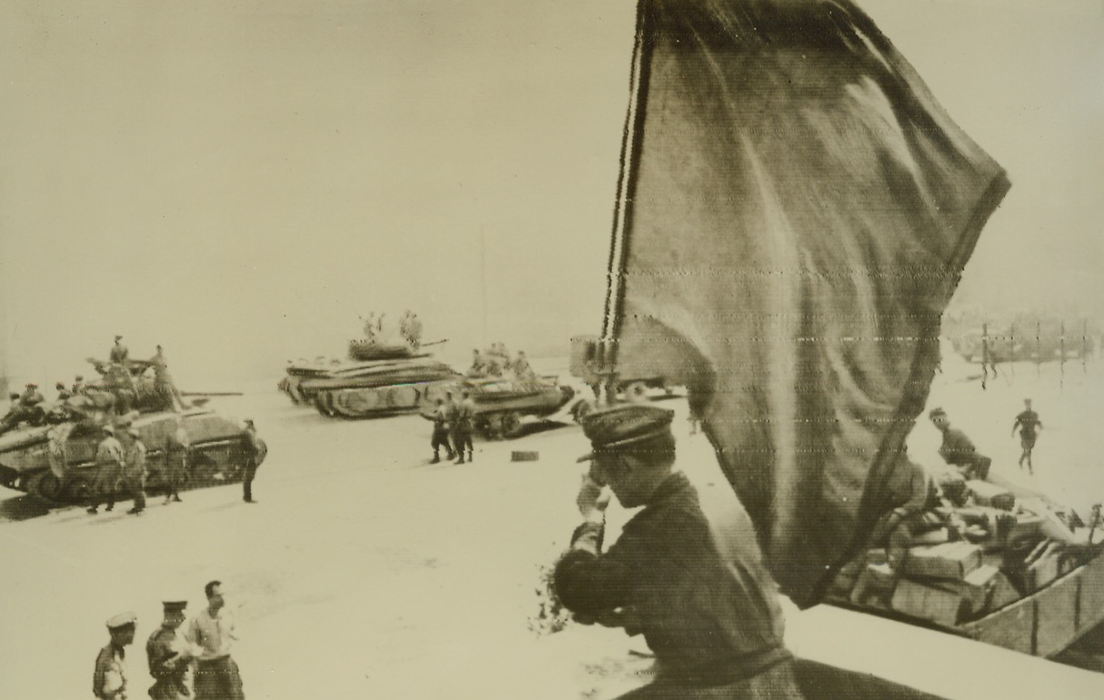 Minsk Loses Nazi Bombs, 7/6/1944. Minsk—Tanksmen stand and watch as the Red Flag of the Soviet Union is raised once more over the industrial city of Minsk. Russian armies rolled forward with terrific speed to retake the city which had become a key Nazi bastian.  Credit: ACME radiophoto.;