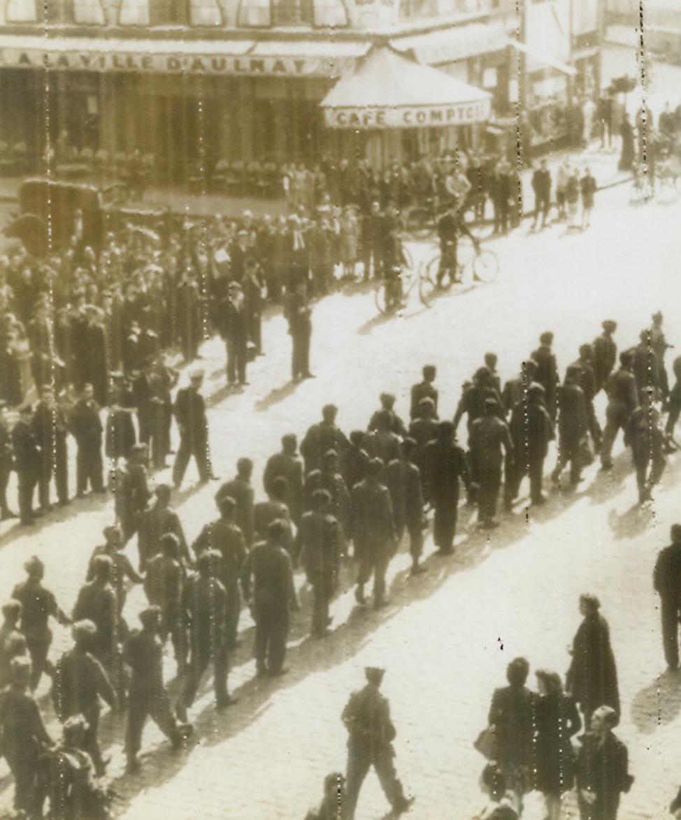 Allied Prisoners March Through Paris, 7/11/1944. According to the German caption accompanying this photo, radioed today (July 11) from Stockholm, these are American and Canadian prisoners from Normandy marching through German-held Paris. Probably as a retaliation for Allied pictures of German prisoners reaching England, the Nazi propaganda line on this photo blares out, in highly sarcastic tone, “the liberators marching through Paris.”  Credit: ACME radiophoto.;