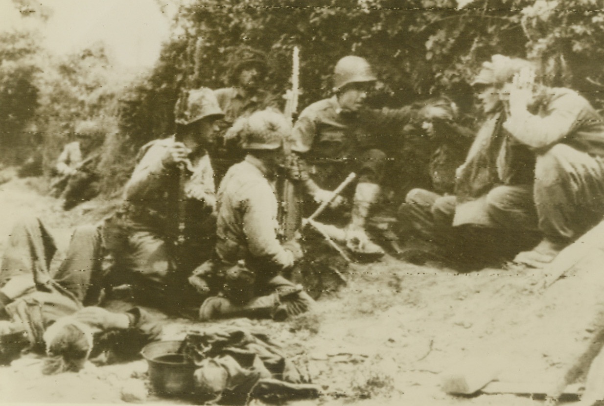 Duck, Nazi, Duck, 7/2/1944. St. Lo, France – Unwilling to meet death, or even injury, at the hands of their own countrymen, the three German prisoners at right hold their ears and duck as Nazi artillery fire blasts over the hedge behind which they and their Yank captors are hiding. A fourth prisoner, who is wounded and has been given first aid treatment, lies at left. Credit: ACME Radiophoto;