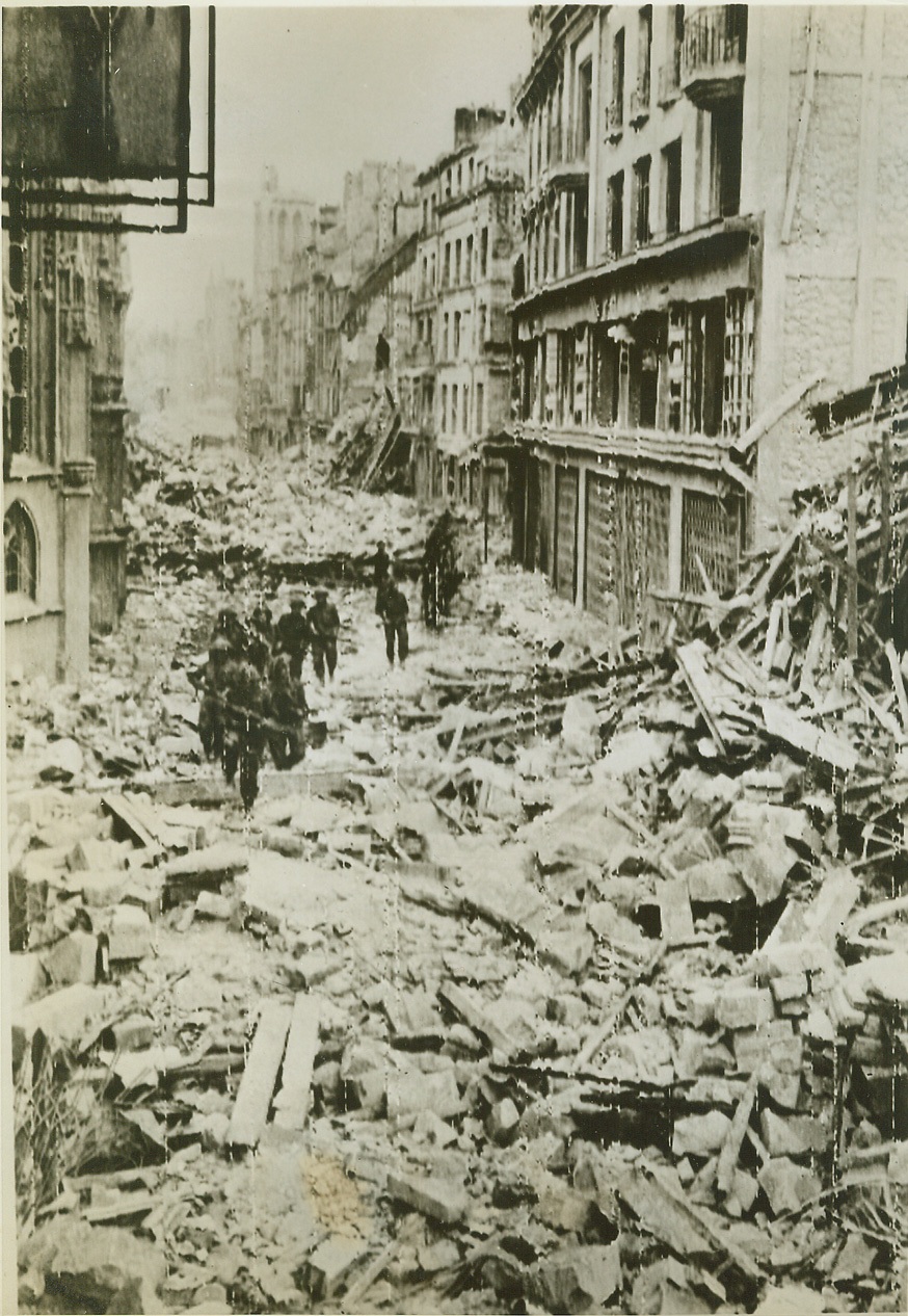 Shambles At Caen, 7/11/1944. France—Its streets filled with the rubble of blasted buildings, Caen presents a desolate picture to Canadian troops entering the city after its capture last July 6th. Here, they advance in single file, their guns ready for instant use against snipers. Today, Germans counterattacked viciously in the Caen sector, temporarily slowing the Allied advance.  Credit: Canadian Army photo via U.S. Army radiotelephoto by ACME;