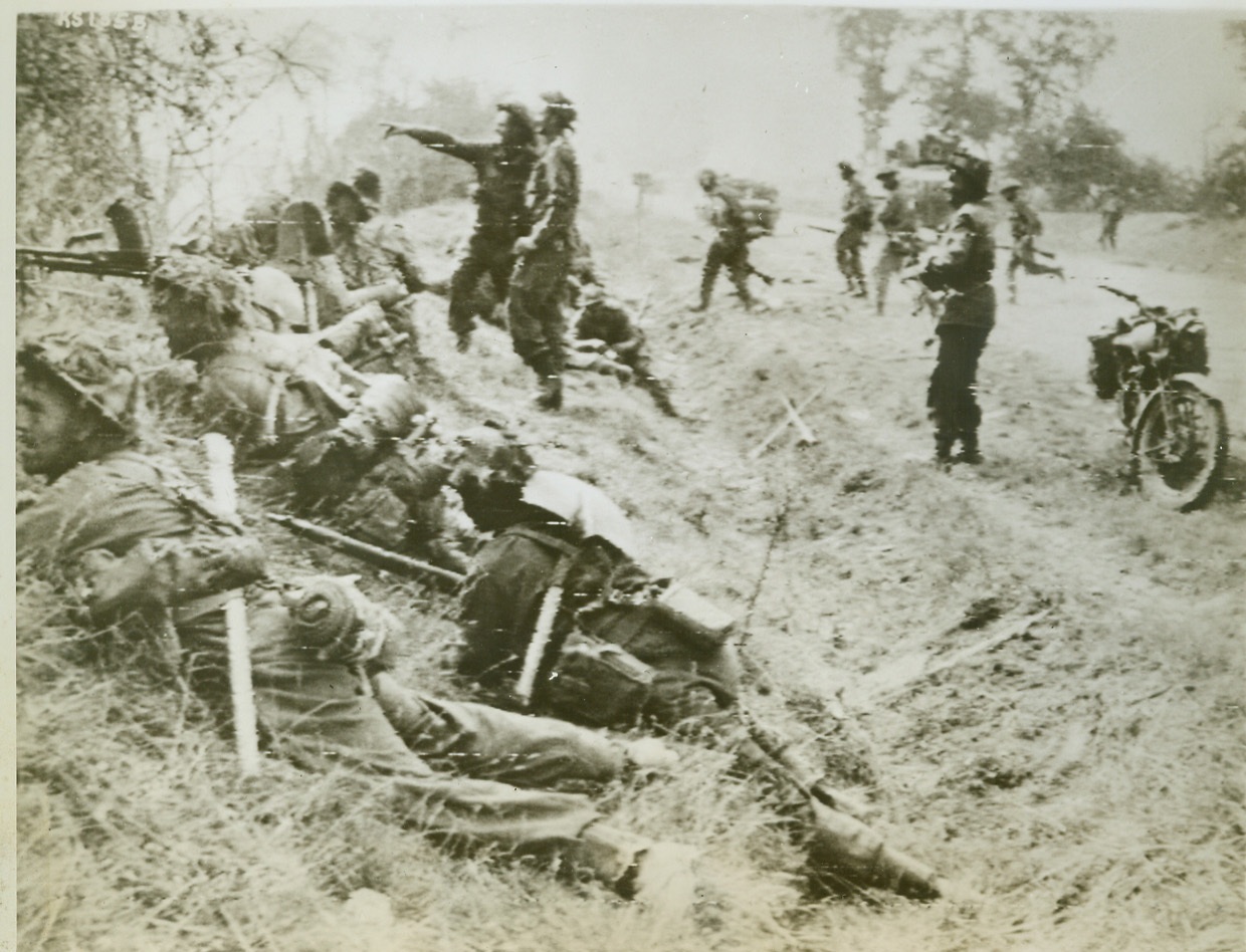 British Attack During Caen Break Through, 7/21/1944. France—Using a ditch for cover, a group of British soldiers attack from a roadside near Cagny, France. Attack was part of the great break through beyond Caen.  Credit: British war office photo via Signal Corps radiotelephoto from ACME;