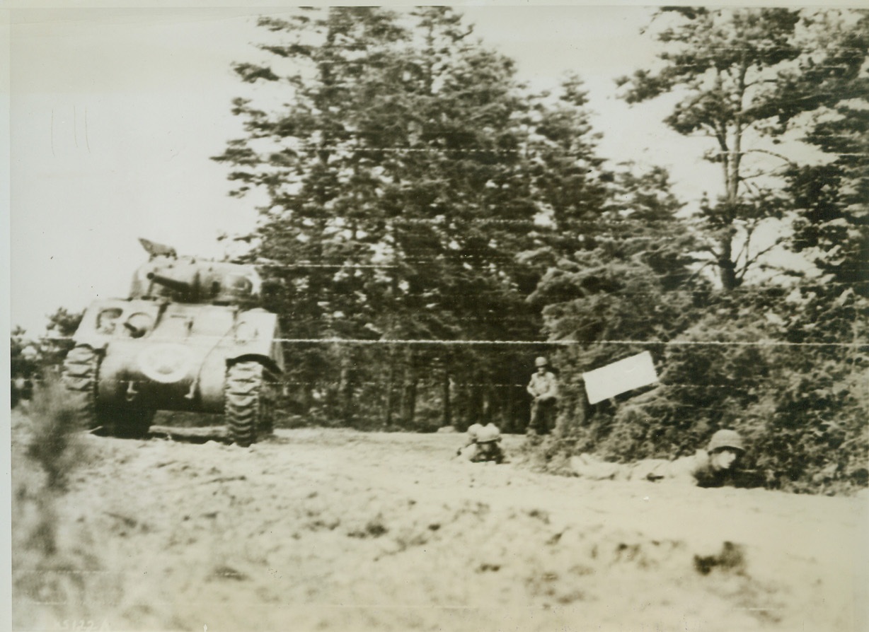 Allies Advance Under Nazi Gunfire, 7/10/1944. France—Crawling slowly along a hedge, two Allied infantrymen advance under Nazi gunfire near St. Jores, France. Tank at left rolls forward to engage the enemy in battle. Photographer inches ahead of advancing troops to make this dramatic picture. Credit: Signal Corps radiotelephoto from ACME;