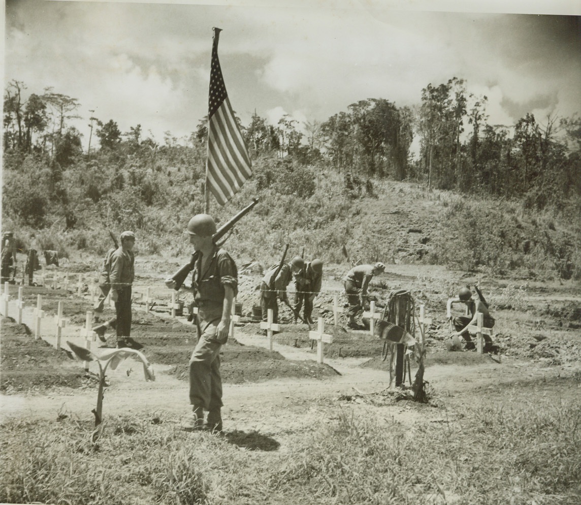 Sentry for Protection, 8/6/1944. Lorengau, Manus Island – Pacing up and down beside the American cemetery at Lorengau, Manus Island, in the Admiralty group, this sentry protects men working on the Yank graves in background. A few hours before, a Jap sniper had picked this spot to strike at American fighters as they set up crosses to mark the graves of their buddies.  Credit: (ACME Photo by Thomas L. Shafer, for the War Picture Pool);