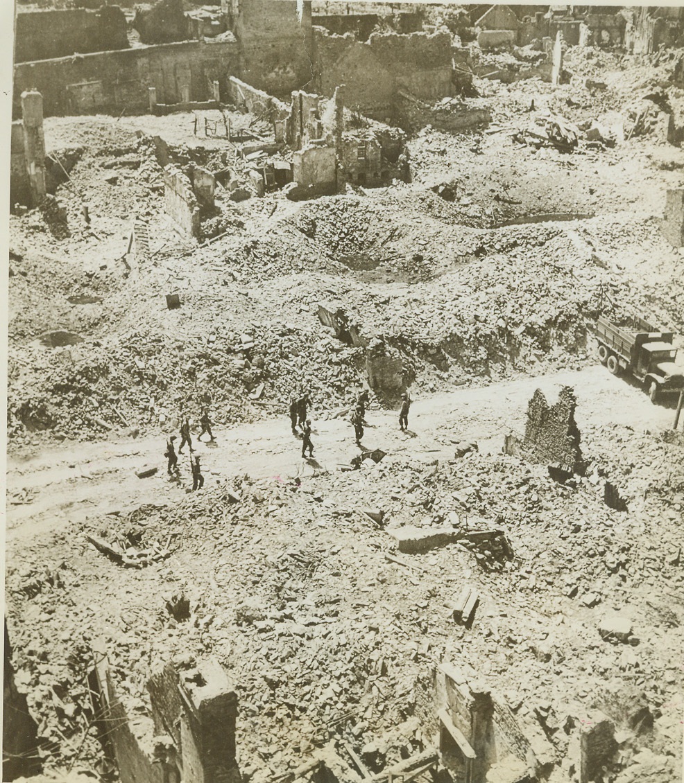 Bomb-Torn St. Lo Plays Host to Yanks, 8/12/1944. ST. LO, FRANCE -- It was a victory in ground gain only for American troops which took St. Lo. Practically all of the city was in the same condition as the section shown here. Soldiers amble down the street looking to both sides, where, stretching as far as the eye can see, is rubble and debris from shattered buildings and emplacements. Credit (ACME) (WP);