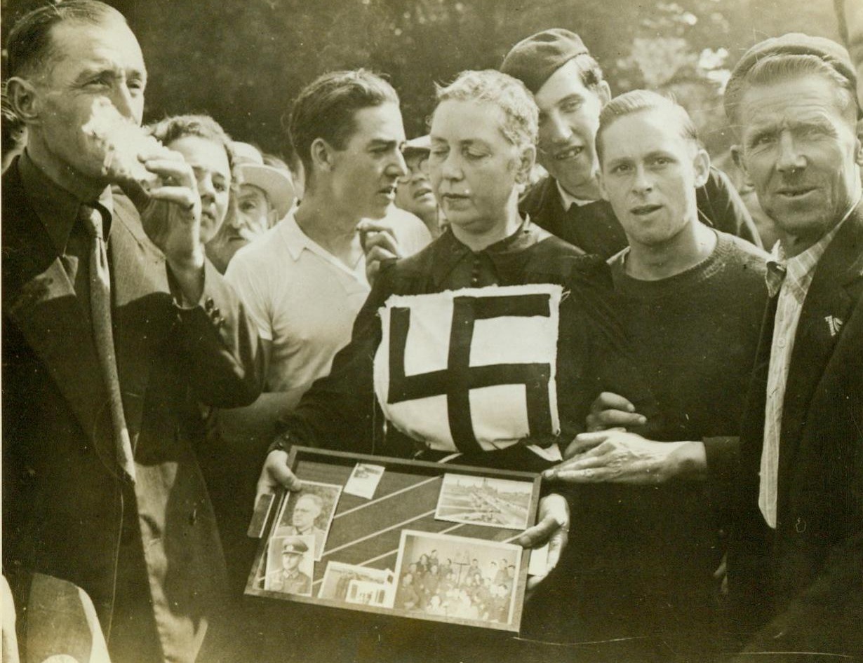 Traitor's Shame, 8/21/1944. Laval, France -- Collecting jeers from the populace, this French girl keeps her eyes on the ground as she is led through the town of Laval by local patriots. Her shorn head and the swastika pinned to her dress mark her as one who collaborated with the Nazis. She carries evidence of her shame in a small tray. The photos of Nazi officers with whom she was friendly were evidently found in her possession.  8/21/44 (ACME);