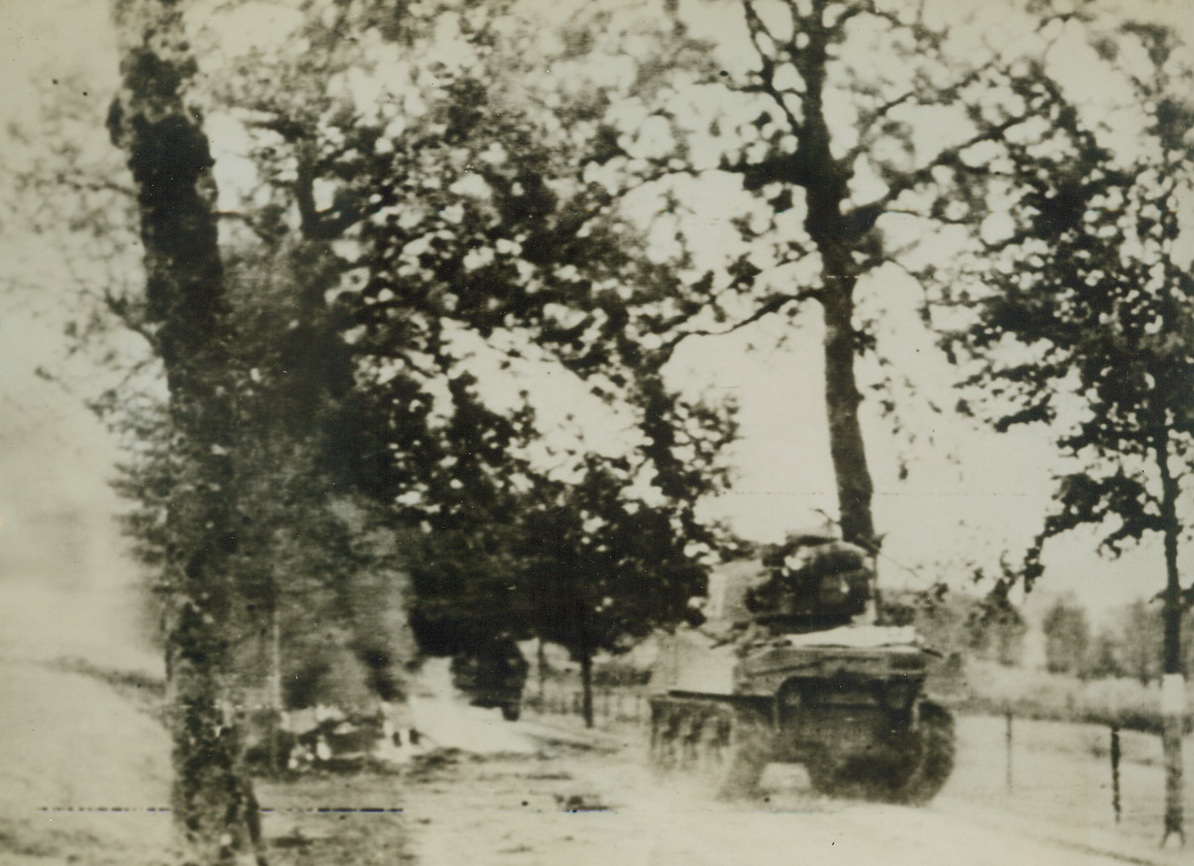 TANKS ADVANCE IN LUXEMBOURG, 9/13/1944. LUXEMBOURG—A United States Sherman tank rolls onward past a destroyed and still burning German vehicle after an encounter just inside the Luxembourg border. Credit: Army radiotelephoto from Acme;