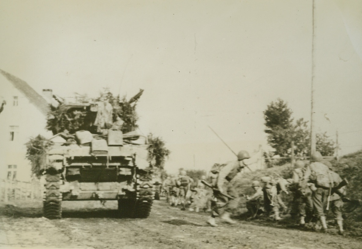 Safety is Where you Find It. 9/19/1944. GERMANY – Yank infantrymen run from behind a tank under a hail of Nazi bullets seeking cover of embankment. Troops were part of huge force now fighting inside Germany. Credit (Army Radiotelephoto from Acme);