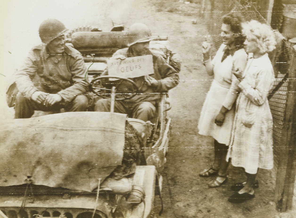 Yanks Hunt Eggs (CQ) in France, 9/8/1944. France—Holding a lettered board written in French and meaning “have you any eggs?” two Yanks ride in a Jeep and hope for a positive answer from French girls in the city of Rumegies, France. Driver and sign holder is Pvt. Maury Sanders of Corinth, Miss. The other Yank, Pvt. Albert Frank, Burlington, VA., looks on.  Credit: Army radiotelephoto from ACME.;