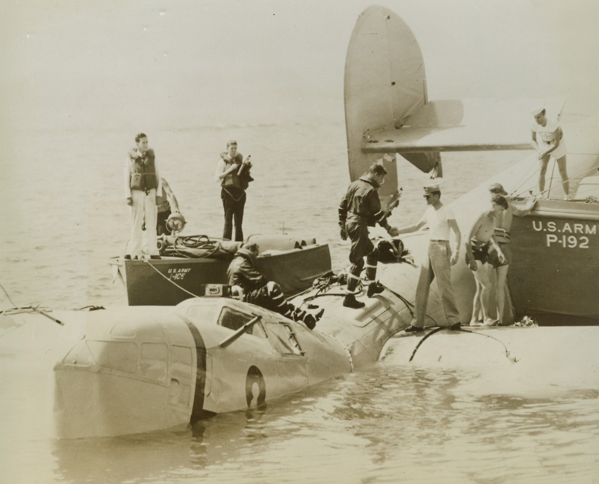 Escape Death in B-24 Experiment, 9/22/1944. Newport News, Va.—Two United States Army Air Forces Airmen almost lost their lives while landing a B-24 Liberator bomber on the James River during an experiment designed to provide improved safety devices for flyers in emergency water landings by land-based aircraft. The plane broke in two but the flyers escaped injury. Maj. Julian A. Harvey (standing, in flying clothes) is congratulated by a fellow officer after the landing. The other member of the crew, Col. Carl F. Greene, can be seen climbing through the escape hatch in the roof of the plane. Credit: ACME.;