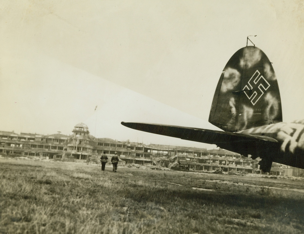 LE BOURGET AIRPORT BATTERED, 9/3/1944. PARIS – Le Bourget airfield, world-famous Paris flying field, battered as the allies advanced to liberate it from the Germans, lies a mass of wrecked hangars and buildings.  The field itself is rutted in places where shells landed.  On the right the tail of a wrecked Messerschmitt 110 just out. Credit: Acme;