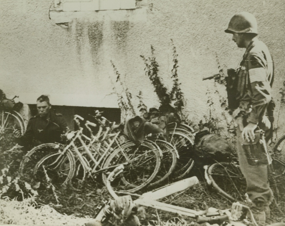 TAKE NAZI PRISONERS AND ESCAPE VEHICLES, 9/13/1944. FRANCE—A German soldier emerges slowly from his hiding place under the pistol point guard of 1st Lt. John W. Upchurch of Chicago, Ill. Nazi had taken refuge in the cellar of a house in Oisulay, France. Bicycles were those stolen by Germans in futile effort to flee the advancing Allies. Credit (Army Radiotelephoto from ACME);