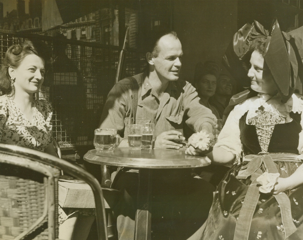 ”Business as Usual”, 9/12/1944.  Lyon, France -- After snipers had been driven from the rooftops in Lyon, and the city had been completely liberated, civilians once more returned to their normal lives, which included tete-a-tetes in their numerous sidewalk cafes. Lt. John Whelden, Newton, Massachusetts, chats over a glass of ale with a buxom French girl, who is attired in traditional peasant costume. Credit: ACME photo by Sherman Montrose, War Pool Correspondent`;