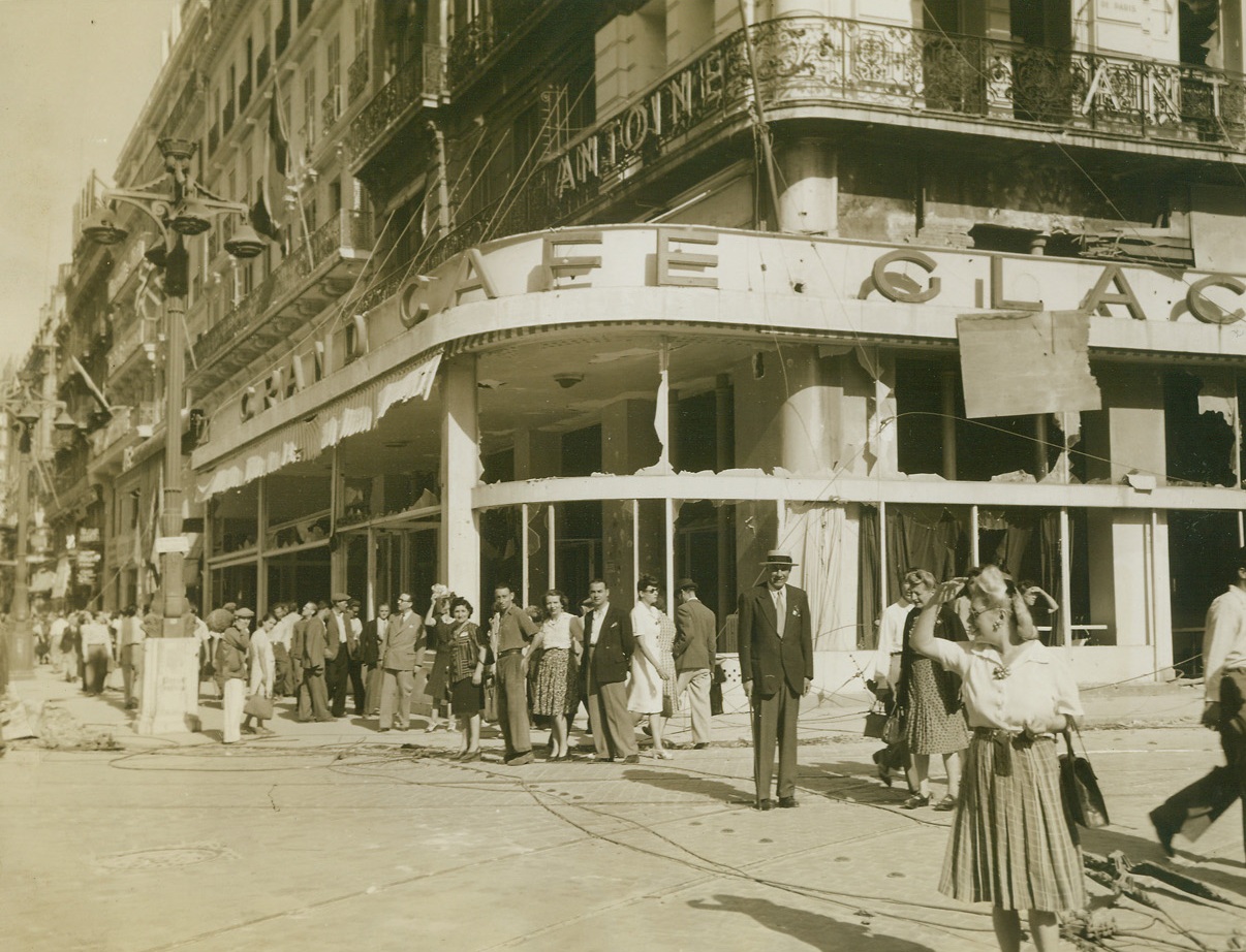 War-Torn Marseille, 9/6/1944. France - Residents of the French city of Marseille walk down famous Canebiere beneath a building that shows the signs of warfare and the results of German artillery fire after the 14 day siege that led to the city’s liberation. The charming blonde French girl in foreground, however, wears what seem to be latest fashions and cuts a mean figure in this war-torn street. Credit: ACME photo by Sherman Montrose, War Pool Correspondent;