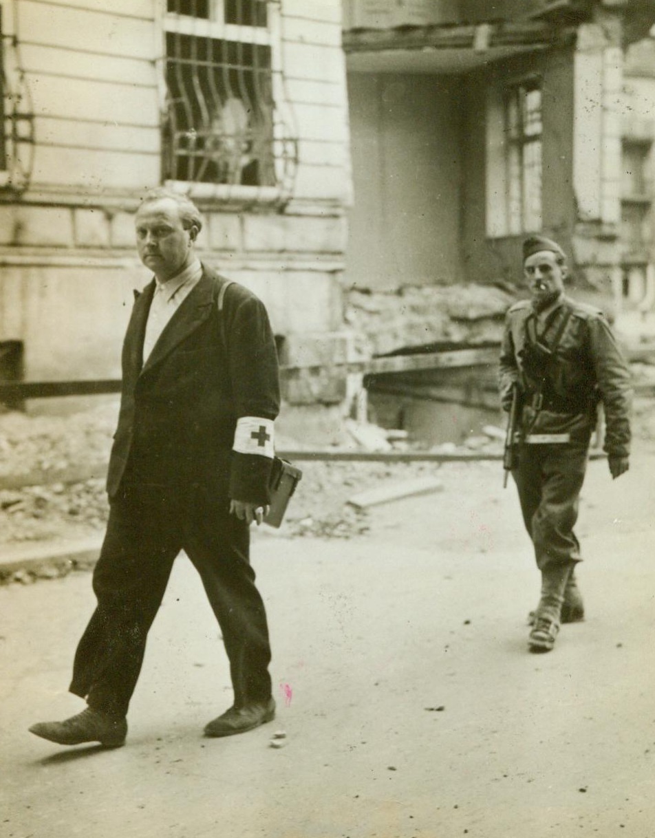 Brother, You’ll Be Sorry, 9/23/1944. Thionville, France - It’s a sad day for this German prisoner, being marched at the gun point of an American soldier down the Adolph Hitler Platz in Thionville. Donning civilian clothes with a Red Cross armband attached to his sleeve, the German went about his sniping until he was finally caught. Under the rules of war, any soldier who is captured wearing any dress other than his uniform, may be condemned to death. Credit: ACME;