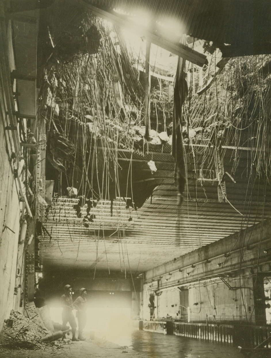 Brest U-Boat Pens Finished, 9/26/1944. Brest, France – Two Allied soldiers stand in one of the Nazi U-boat pens at Brest and look at the gaping 40 foot hole made in the roof. Dirt and grass which formed the camouflage cascades down the hole. Although built of thick reinforced concrete, several direct hits blew in the roofs of three pens. Credit: British official photo from ACME;