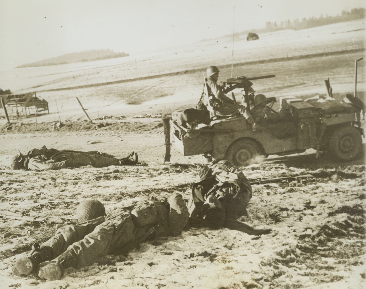 DOWN AS THEY BATTLED GERMAN ATTACK, 1/8/1945. CHAUMONT, BELGIUM—Killed as they tried to ward off the German counter-offensive launched at Chaumont, five miles south of Bastogne, these American soldiers lie where they fell in the snow. On the right, three Yanks in a jeep keep on the alert for other enemy attacks. Gen. Patton’s army, which relieved besieged Bastogne, has succeeded in narrowing the neck of the German bulge to less than 10 miles. Credit: Acme;