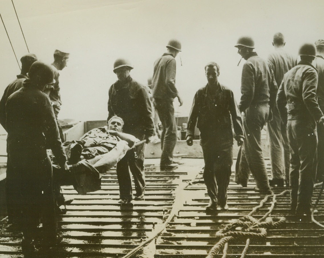 First Casualty of Ryukyus Assault, 4/7/1945. Pacific -- An American soldier of the 10th Army’s 77th division is carried by Coast Guardsmen through the big bow doors into the tank deck of an LST taking part in assault on Islands in the Ryukyus.  Soldier was first reported casualty of invasion of the island chain just below Japan.  He was wounded by a Jap sniper on beach of Aka Shima in the Keramas.Credit Line (Coast Guard photo from ACME;