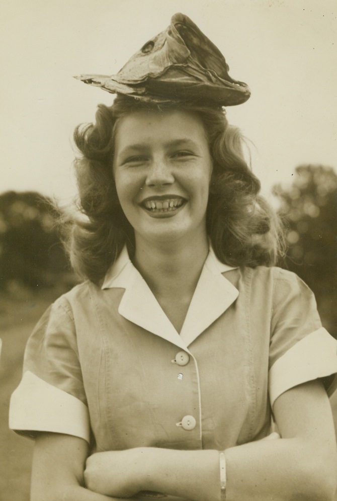 Looks Fishy, 7/13/1945. Lake James, N.C.—If this poor fish had known enough to keep his mouth shut, he would never have wound up as a hat. But he didn’t, so consequently Helen Steele, Asheville, N.C., has a fragrant new hat. The bass was caught in Lake James, N.C., by a fisherman friend of Helen’s. Credit: ACME.;