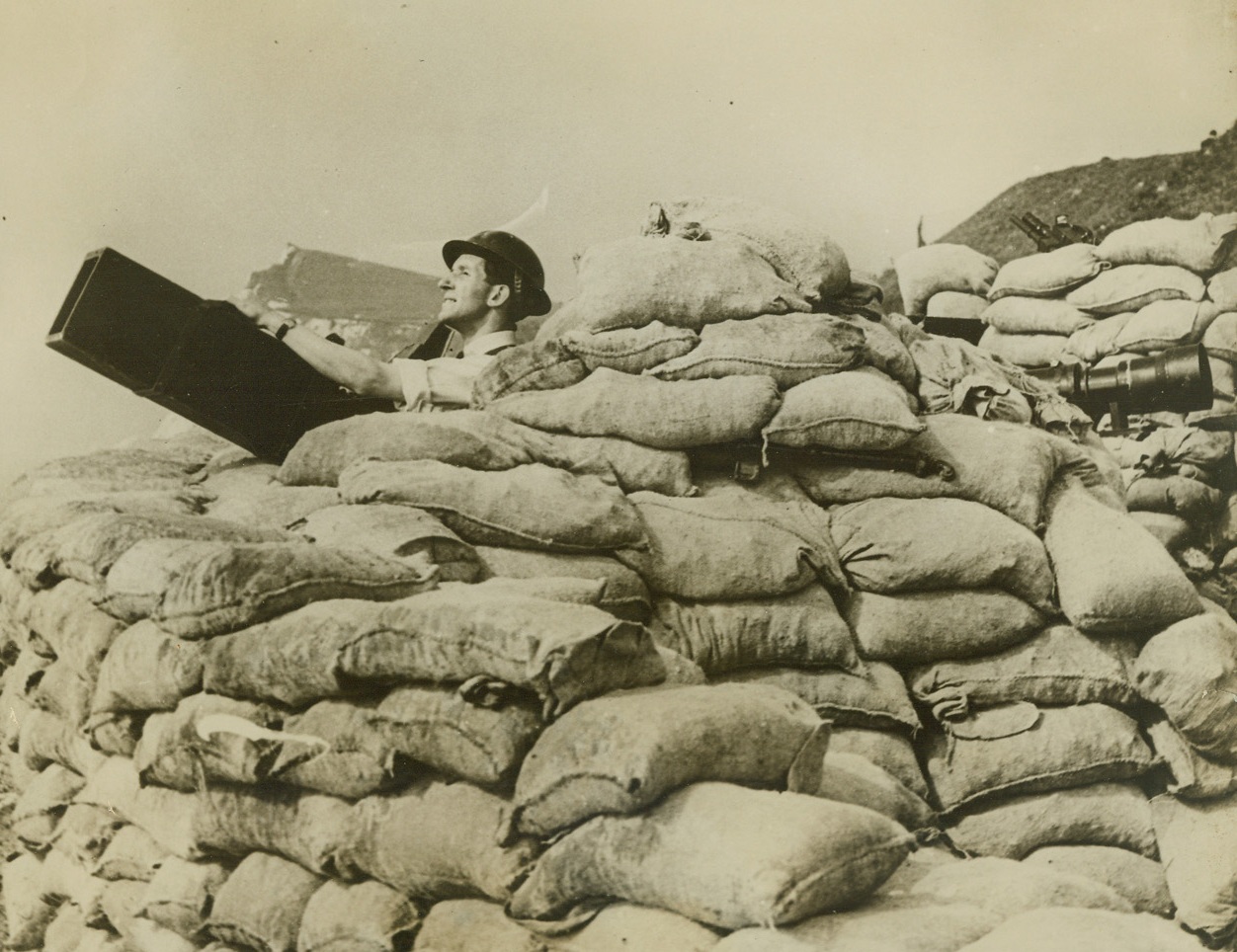 ACME PHOTOGRAPHER “SHOOTS” WAR FROM SANDBAGS, 10/1/1940  DOVER, ENGLAND – H.P. Andrews, Acme newspictures staff photographer in England, operating a long focus camera from a sandbag emplacement on the Dover Cliffs, from where can be had a “grandstand” view of the war along Britain’s Southeast coast.  Andrews wears a steel helmet for additional protection. Credit: Acme;