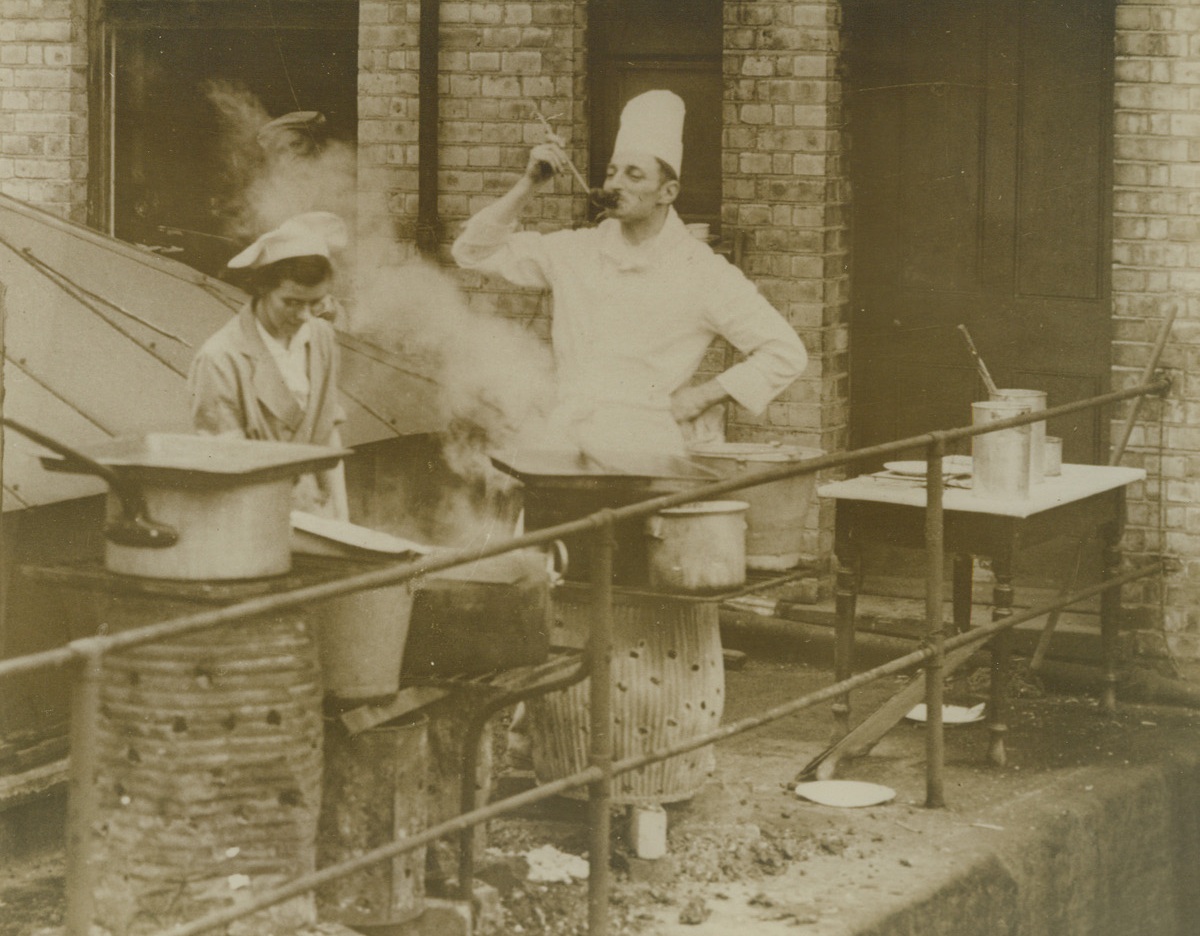 Field Kitchen On London Roof, 10/11/1940  London – Chef Parkes sampling one of the meals he prepares in a field kitchen on the roof of a well-known London store. Despite the interruptions of air raid alarms, Chef Parkes is preparing lunches for hundreds of the store’s customers. He whips up a four-course meal in this improvised kitchen. Credit: ACME;