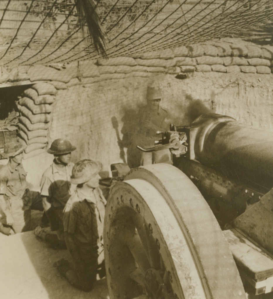 British Guns Boom on the Desert, 12/26/1940  Smoke pours from the breech as a British heavy field gun speaks from its camouflaged emplacement on the Western Desert. Artillery of all types played an important part in recent British successes against Italian forces on the desert. Credit: ACME.;