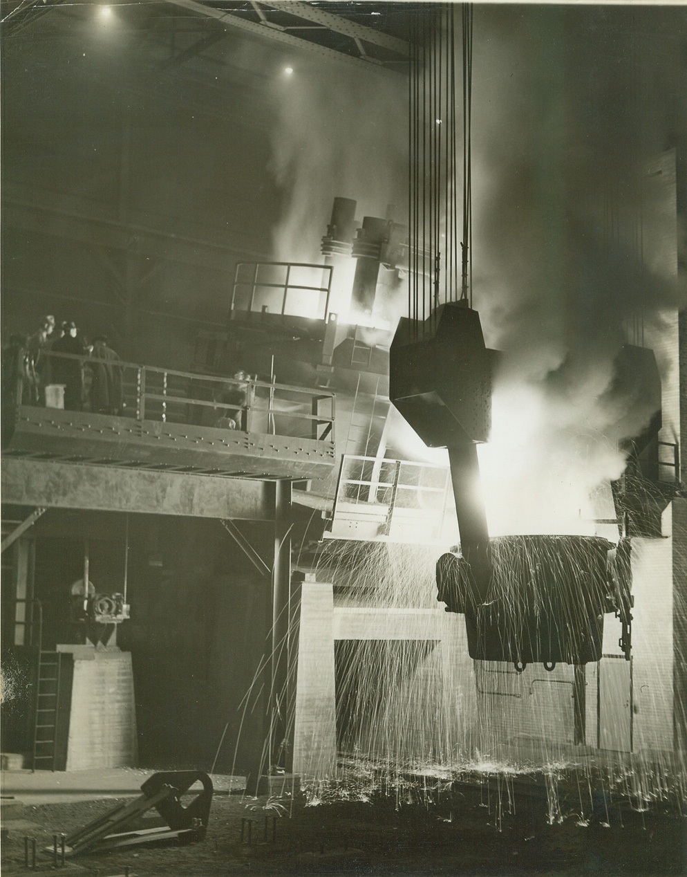 BIGGEST PRODUCER DOUBLES STAINLESS STEEL OUTPUT, 10/28/41  CHICAGO, IL—Maj. General Joseph Cummins, Commanding of the Sixth Corps area, and other defense officials (on the platform at left) watch the first pouring from one of two new electric furnaces installed in the corporation. Their output of 100,000 net tons annually doubles the previous output, and makes the plant the greatest producer of stainless steel in the United States. In the glare above the furnace (upper center) can be seen the giant electrodes that produce the intense heat necessary in making the alloy. Credit: OWI Radiophoto from ACME;