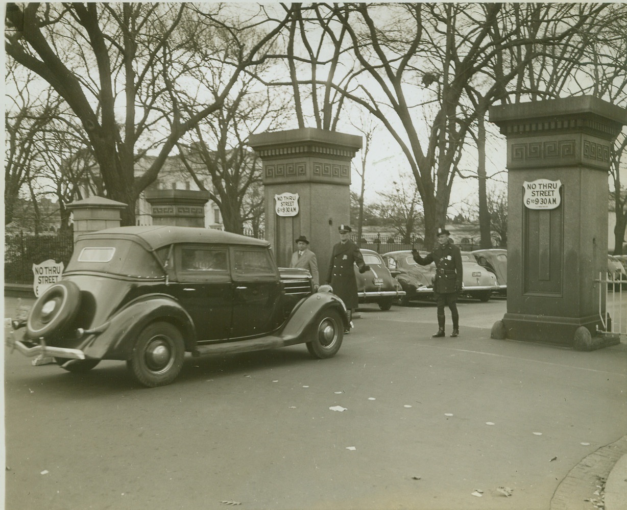 Traffic Routed Around White House, 12/9/41  Washington, D.C.—Streets circling the White House grounds have been blocked off and all cars seeking entrance are stopped for inspection. Only those on official business are permitted to enter. Photo shows metropolitan police on guard at the west executive barrier (West Executive Avenue) halting a motorist, Dec. 9. White House is shown in left background. Credit: ACME.;