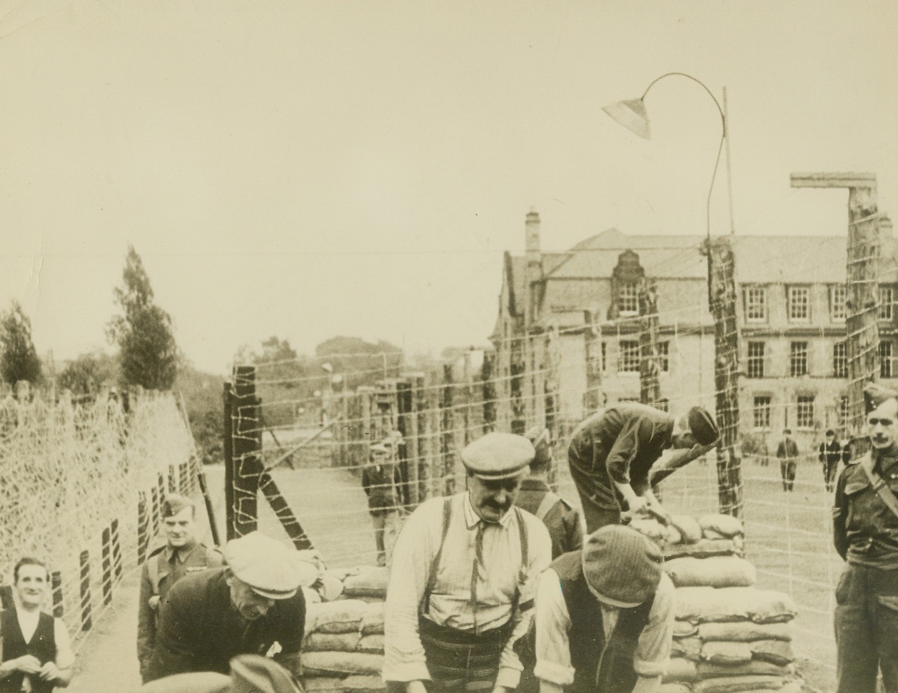 Air Raid Shelter for German Prisoners of War, 11/9/1939. Somewhere in England – While workmen in the foreground build an air raid shelter for their protection in case German bombers should drop their “eggs” in the vicinity, German prisoners of war can be seen exercising on the grounds of a large country mansion where they are interned for the duration. This picture, one of the first to be made of German war prisoners, who included members of German U-Boat crews, was rushed to the United States via Trans-Atlantic Clipper. Passed by Censor. Credit: ACME;